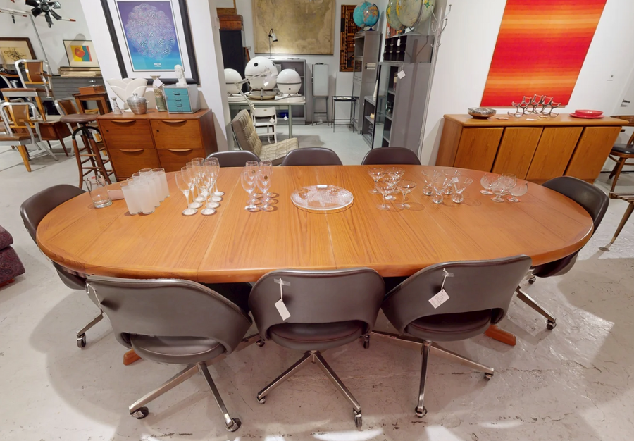 Oval teak dining table with two extension leaves surrounded by chairs